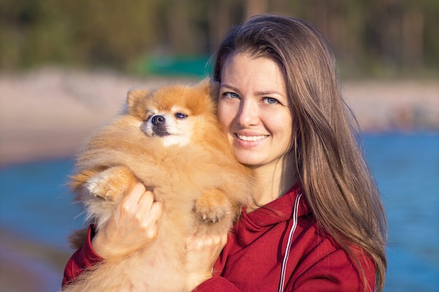 Młoda Kobieta, Przytulanie Psa Szpic Pomorski Na Rękach. Opieka Nad Zwierzętami, Adopcja.