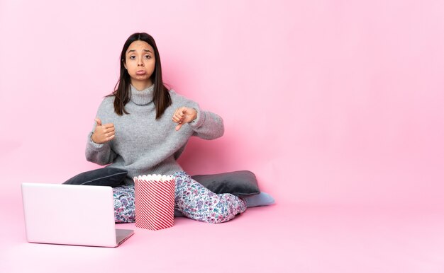 Młoda kobieta rasy mieszanej jedzenie popcornu podczas oglądania filmu na laptopie co dobry znak. Niezdecydowany między tak lub nie