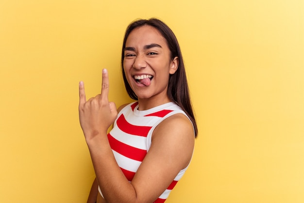 Młoda kobieta rasy mieszanej na żółtym tle pokazujący rockowy gest palcami
