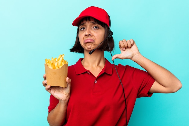 Zdjęcie młoda kobieta rasy mieszanej pracownik restauracji fast food trzymający frytki na białym tle na niebieskim tle czuje się dumny i pewny siebie, przykład do naśladowania.