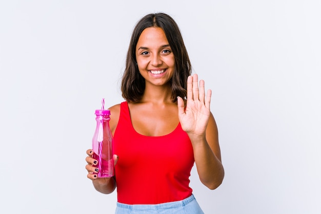 Młoda kobieta rasy mieszanej trzymając shake mleka na białym tle uśmiechnięty wesoły pokazując numer pięć palcami.