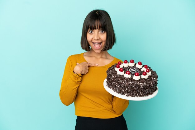 Młoda kobieta rasy mieszanej trzymająca tort urodzinowy z niespodzianką wyrazem twarzy