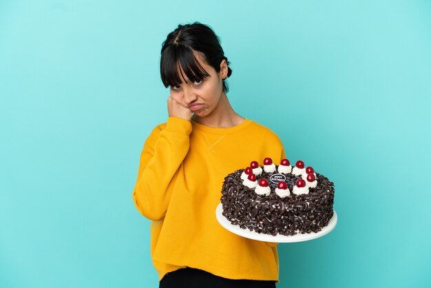 Młoda kobieta rasy mieszanej trzymająca tort urodzinowy ze zmęczoną i znudzoną miną