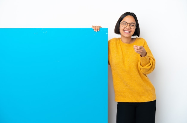 Młoda kobieta rasy mieszanej z dużym niebieskim plakietką na białym tle, wskazując przód z szczęśliwym wyrazem twarzy
