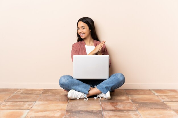 Młoda kobieta rasy mieszanej z laptopem siedząc na podłodze brawo