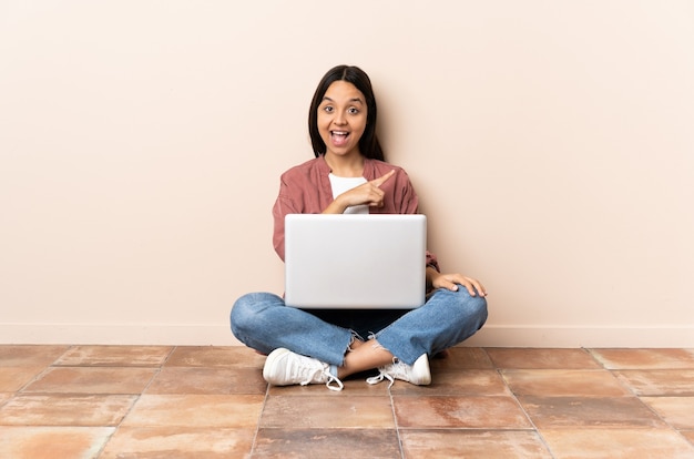 Młoda kobieta rasy mieszanej z laptopem siedząc na podłodze