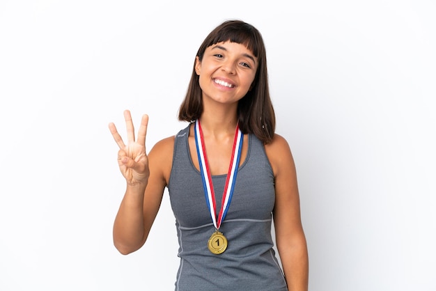 Młoda kobieta rasy mieszanej z medalami na białym tle szczęśliwa i licząca trzy palcami