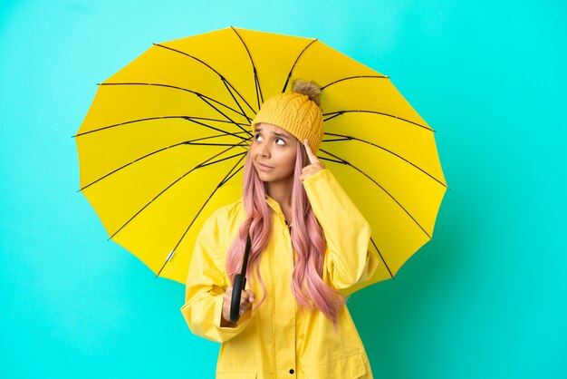 Młoda kobieta rasy mieszanej z płaszczem przeciwdeszczowym i parasolem, mająca wątpliwości i myśląca