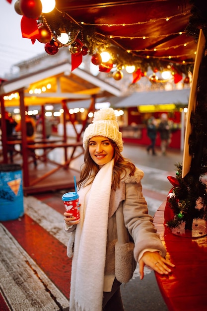 Młoda kobieta relaksująca picie kawy na świątecznym jarmarku bożonarodzeniowym Zimowe wakacje Światła wokół