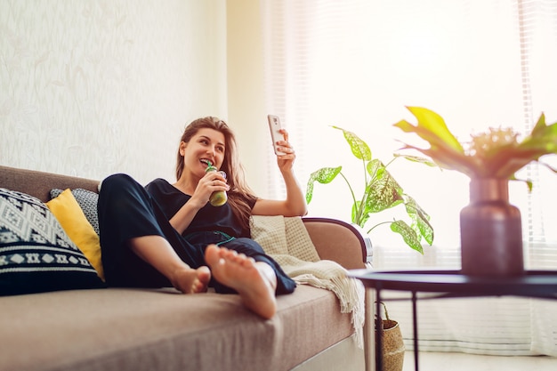 Młoda Kobieta Relaksuje W żywym Pokoju I Pije Smoothie Używać Smartphone. Zdrowa Dieta