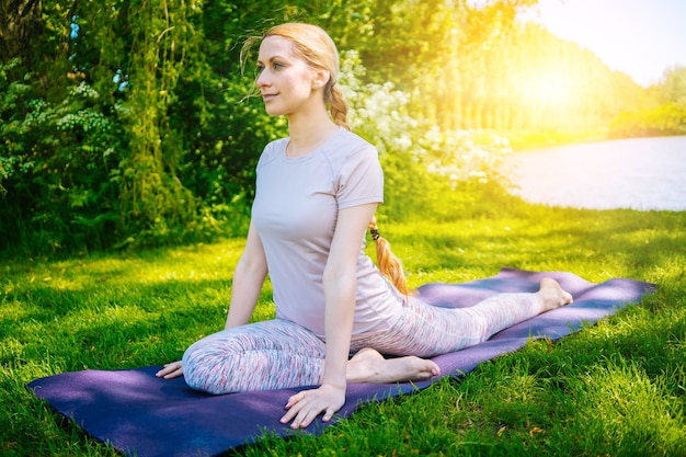 Młoda kobieta robi asanę jogi w parku dziewczyna rozciągająca ćwiczenia w pozycji jogi szczęśliwa i zdrowa kobieta siedzi w pozycji lotosu i ćwiczy medytację jogi i sport na zachód słońca na zewnątrz