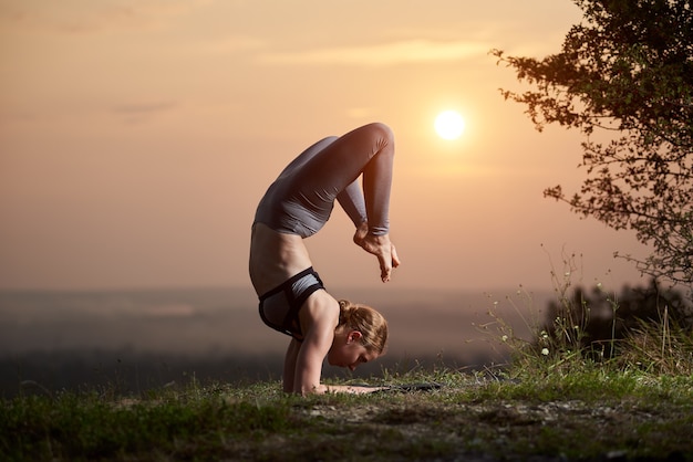 Młoda kobieta robi ćwiczenia jogi na świeżym powietrzu o zachodzie słońca