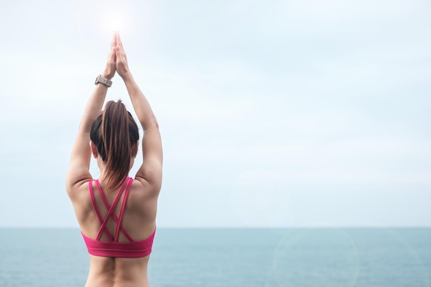 Młoda kobieta robi joga i rozciąganie mięśni rano, zdrowa dziewczyna medytacja przed widokiem na ocean. koncepcje wellness, fitness, witalności, ćwiczeń i równowagi między życiem zawodowym i prywatnym