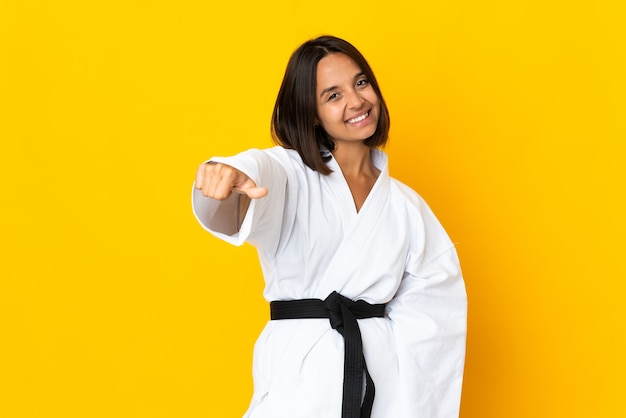 Młoda kobieta robi karate na białym tle na żółtym tle, dając kciuki do góry gestu