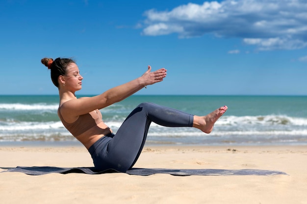 Młoda kobieta robi pilates na brzegu plaży w stroju sportowym