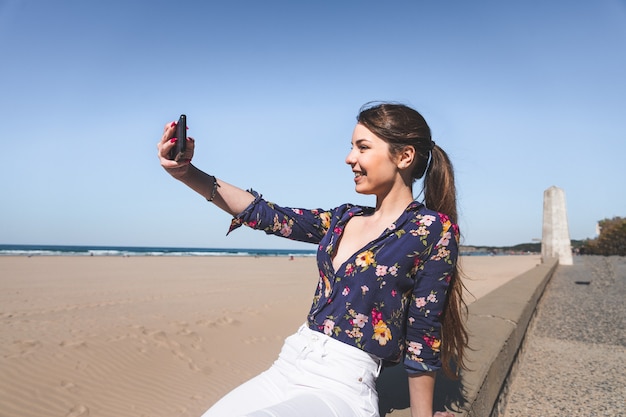 Młoda kobieta robi selfie telefonem komórkowym na plaży