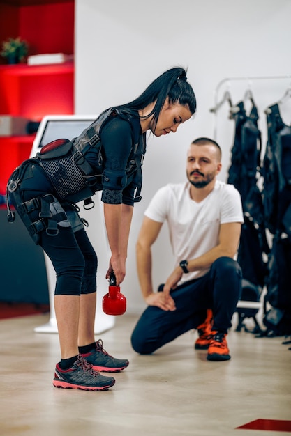 Młoda kobieta robi trening osobisty EMS z trenerem na siłowni.