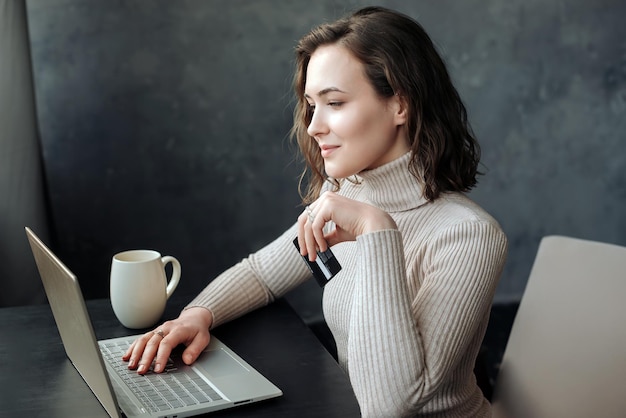 Młoda kobieta robi zakupy online, trzymając kartę kredytową i używając laptopa do transakcji e-commerce