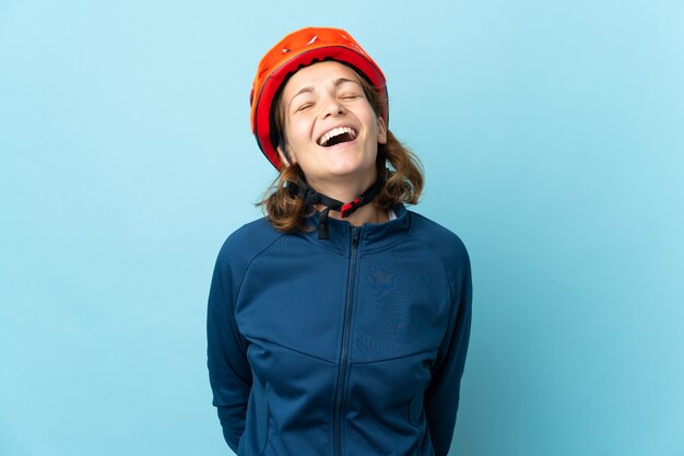 Młoda kobieta rowerzysta na białym tle na niebieskiej ścianie, śmiejąc się