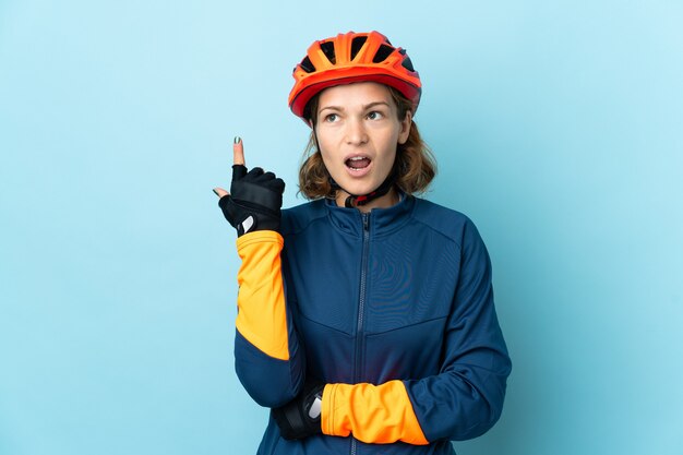 Młoda kobieta rowerzysta na białym tle na niebieskim tle myśli pomysł wskazując palcem w górę