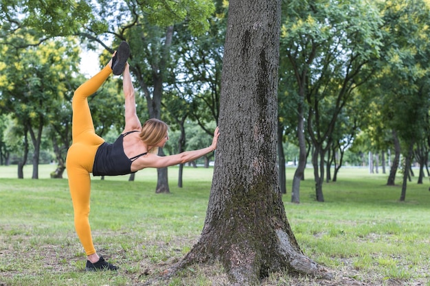 Zdjęcie młoda kobieta rozciągająca i podnosząca nogę bardzo wysoko w parku