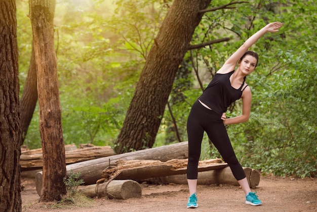 Młoda kobieta, rozciąganie przed bieganiem w zalesionym lesie, szkolenia i ćwiczenia na bieganie w terenie maraton wytrzymałościowy koncepcja zdrowego stylu życia