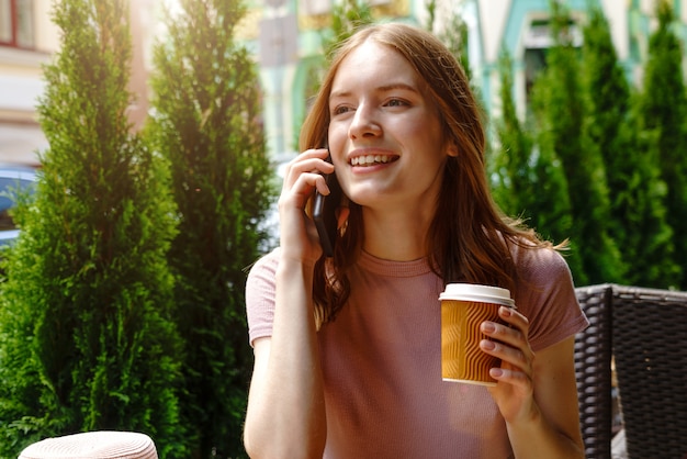 młoda kobieta rozmawia przez telefon w kawiarni na letnim tarasie