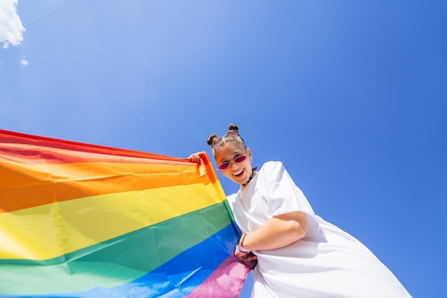 Młoda kobieta rozwija tęczową flagę na tle nieba