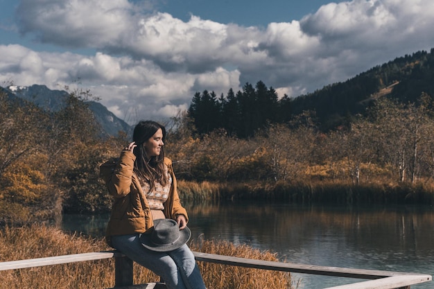 Zdjęcie młoda kobieta siedząca na ogrodzeniu na brzegu jeziora jesienią