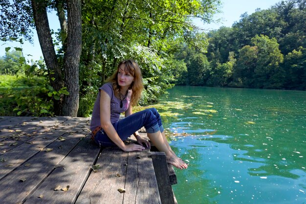 Zdjęcie młoda kobieta siedząca nad jeziorem przy drzewach