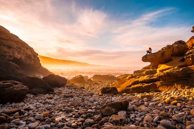 Młoda kobieta siedząca w Orange Sunset na wybrzeżu Góry Jaizkibel w pobliżu San Sebastian, Gipuzkoa. Hiszpania