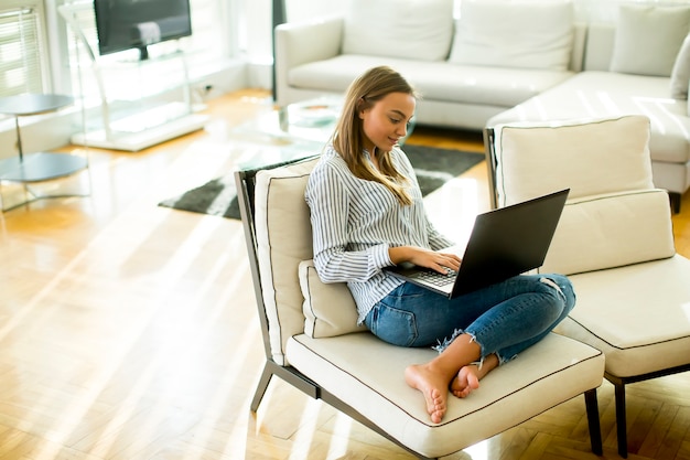 Młoda kobieta siedzi na kanapie w pokoju i za pomocą laptopa