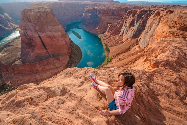 Młoda kobieta siedzi na krawędzi klifu z widokiem na Horseshoe Bend w Page Arizona