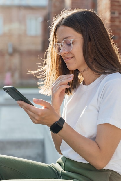 Młoda kobieta siedzi na miejskich schodach i mówi na smartfonie