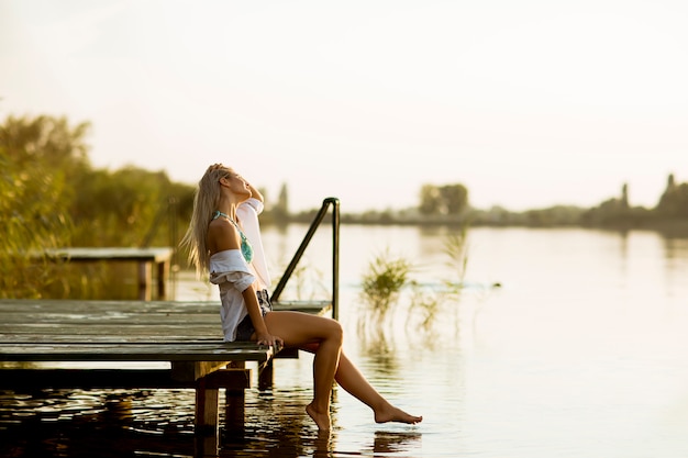Młoda kobieta siedzi na molo nad jeziorem