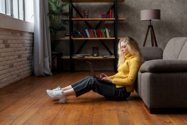 Zdjęcie młoda kobieta siedzi na podłodze w domu i pracuje z laptopem.