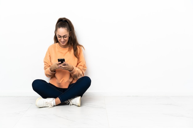 Młoda kobieta siedzi na podłodze, wysyłając wiadomość przez telefon