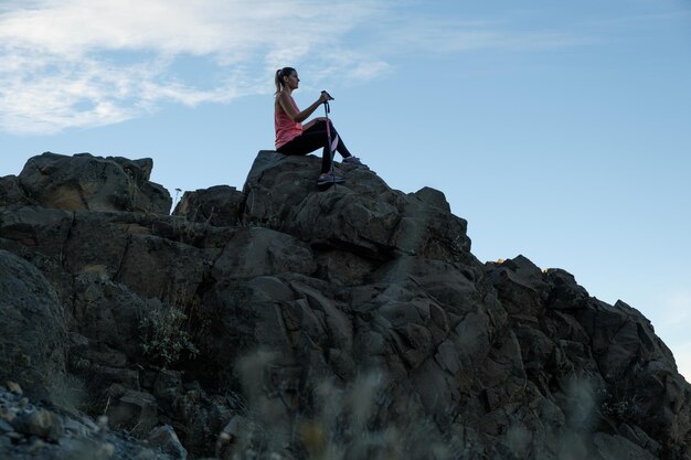 Młoda kobieta siedzi na szczycie góry o zachodzie słońca