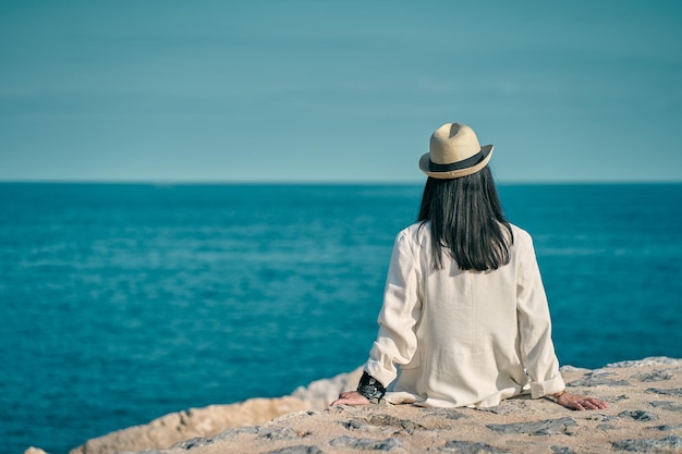 Zdjęcie młoda kobieta siedzi patrząc na morze w kapeluszu
