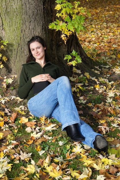 Młoda kobieta siedzi pod drzewem jesienią