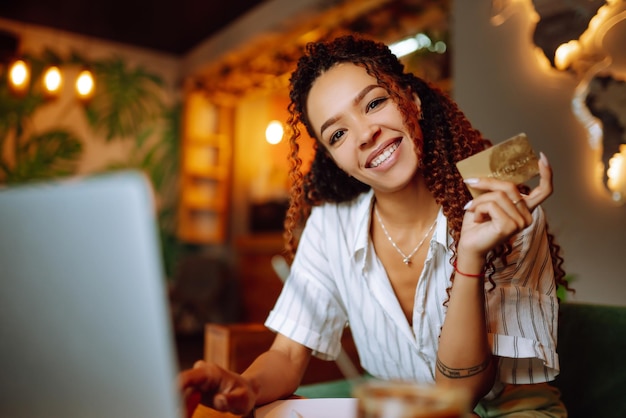 Młoda kobieta siedzi w kawiarni dokonywania zakupów online przy użyciu karty kredytowej i laptopa Zakupy online