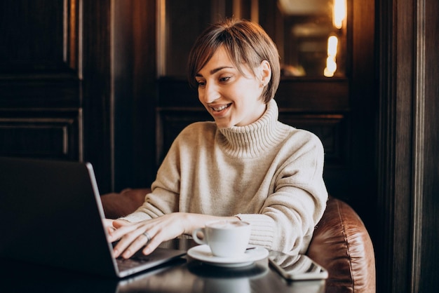 Młoda kobieta siedzi w kawiarni, pije kawę i pracuje na komputerze