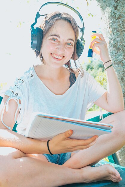 Młoda kobieta siedzi w ogrodzie, uśmiechając się i studiując na uniwersytecie, lubi rekreację na świeżym powietrzu, słuchając muzyki i korzystając z laptopa. Skopiuj miejsce, koncepcja stylu życia ludzi. Pisanie na komputerze