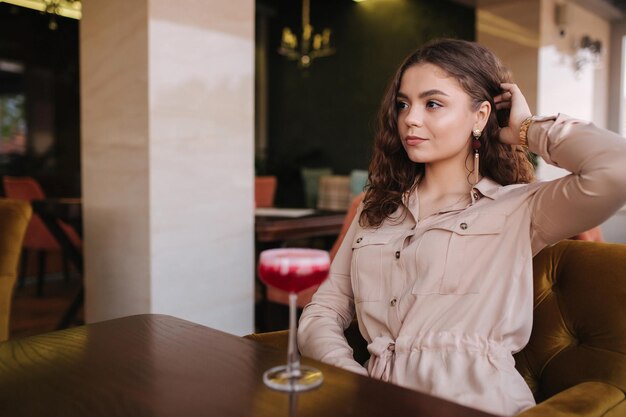 Młoda kobieta siedzi w restauracji i pije koktajl Piękna dziewczyna z uśmiechem kręconych włosów