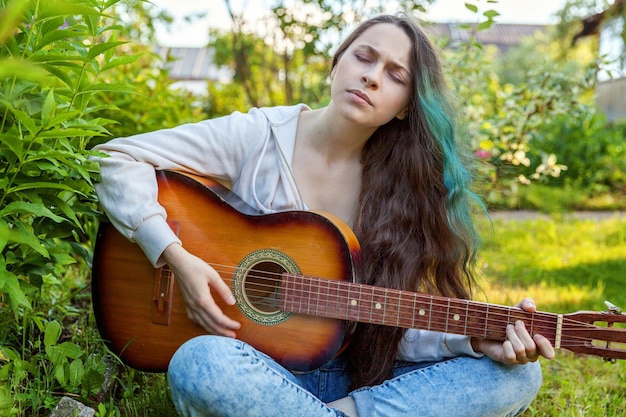 Młoda kobieta siedzi w trawie i gra na gitarze