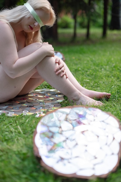 Zdjęcie młoda kobieta siedzi z zawiązanymi oczami na trawniku i odzwierciedla obiekty wokół siebie