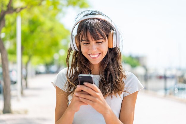 Młoda kobieta słucha muzyki na zewnątrz i patrzy na telefon komórkowy