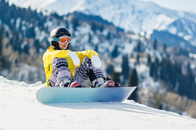 Młoda kobieta snowboardzistka siedzi na śniegu i eksploruje stok przed zjazdem