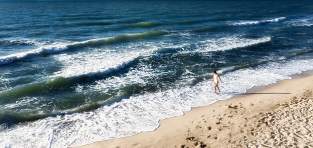 Młoda kobieta spaceru na plaży wzdłuż wybrzeża z błękitną wodą