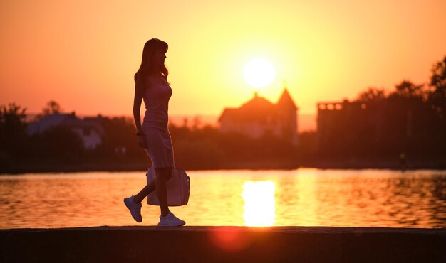 Młoda kobieta spacerująca samotnie po chodniku nad brzegiem jeziora w ciepły wieczór Samotność i relaks w koncepcji natury